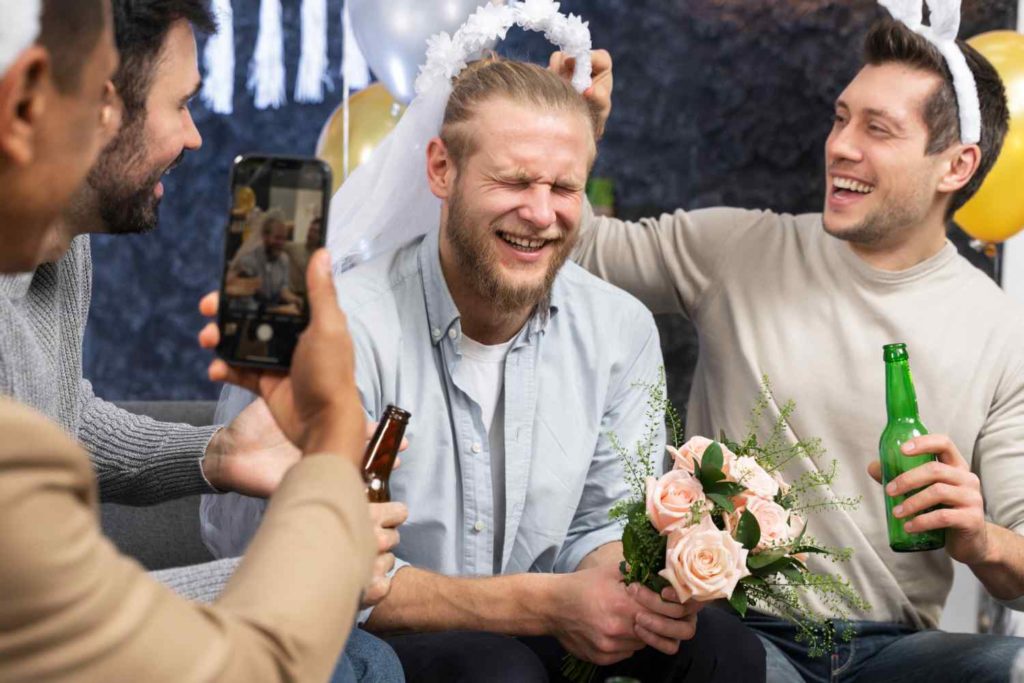 Un hombre sonriente coloca un velo de novia blanco sobre amigo en su despedida de soltero